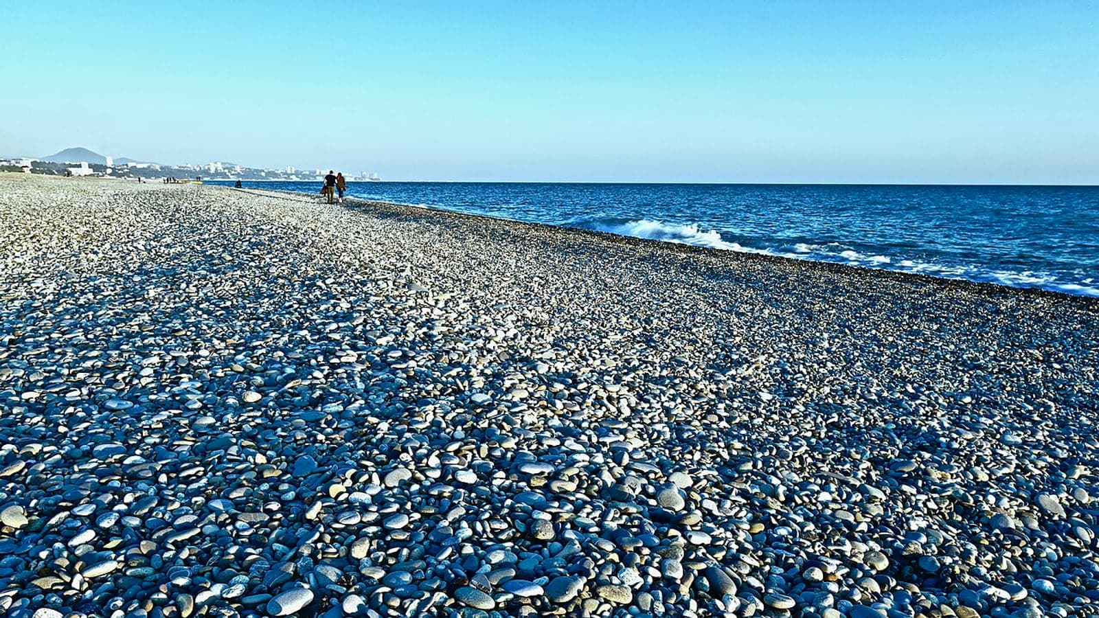 Галечный берег, море и город у подножия гор